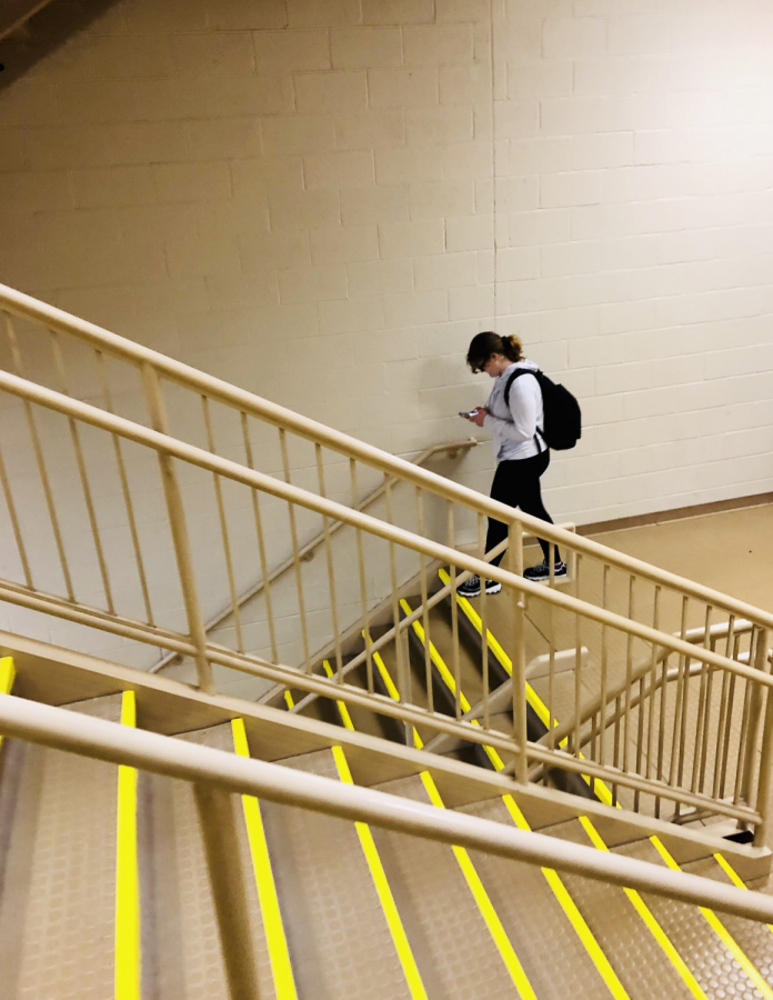 A+Monroe-Woodbury+High+School+student+gazes+intently+at+her+phone+as+she+walks+down+the+stairs.+Students+are+frequently+seen+so+engaged+in+their+electronics+that+they+bump+into+others+or+trip+while+walking+to+their+next+class+in+the+hallways+of+MWHS.