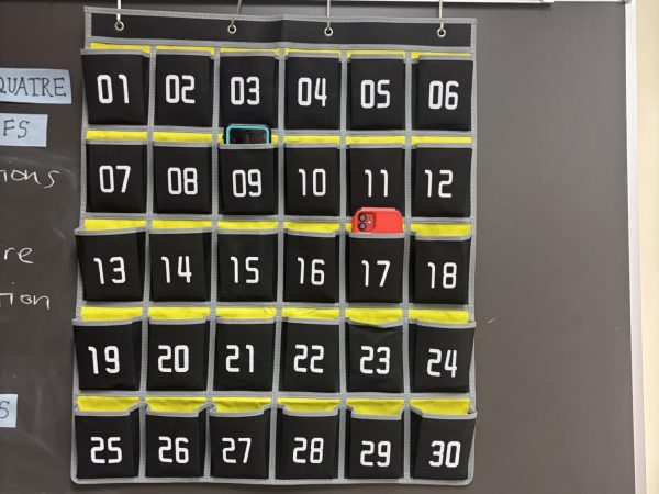 A hanging phone holder, with numbered pockets to hold a cell phone. Two phones are in their pockets.