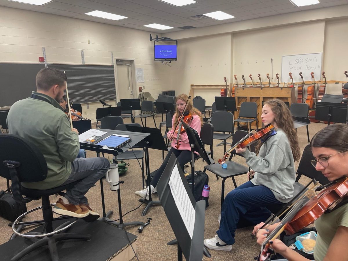 Music teacher Mr. Champlin teaches violin to a group of students in the music room.